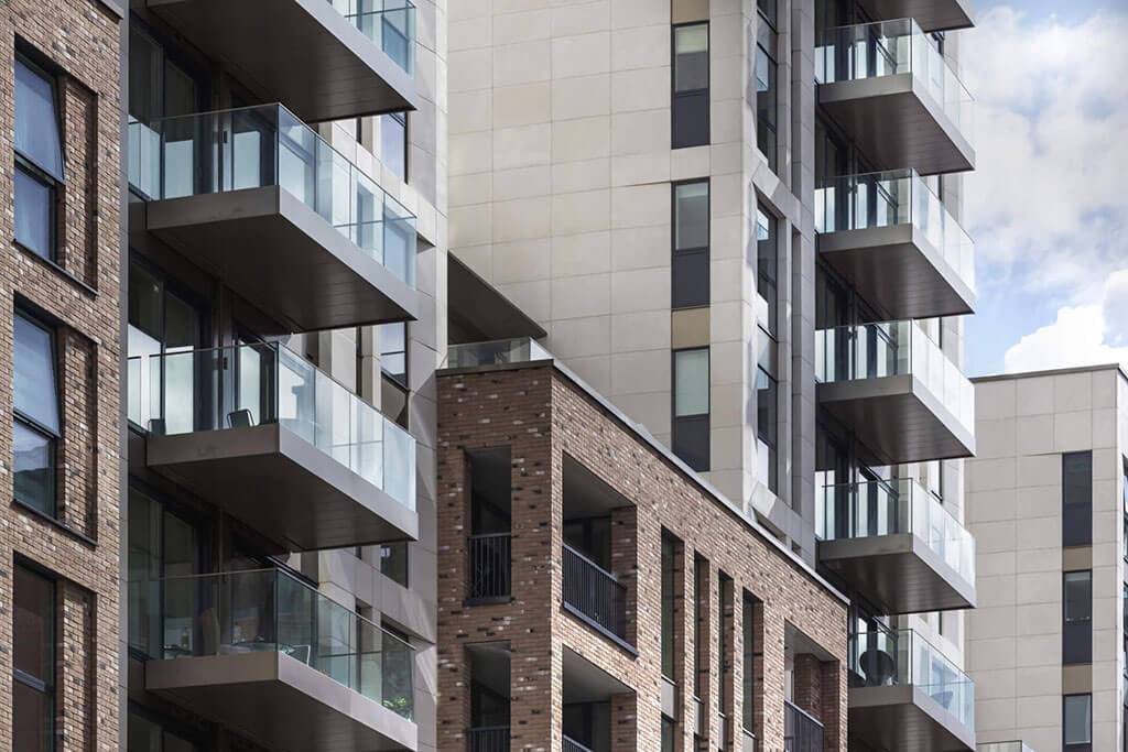 Okna drewniano – aluminiowe, okna balkonowe, kolor antracyt, widok od zewnątrz na budynek apartamentowca, elewacja z cegły i płyt piaskowca, przeszklone balkony.