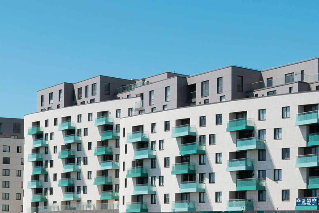 Okna drewniano – aluminiowe, kolor antracyt, widok od zewnątrz, kolor elewacji biały, balkony turkusowe, błękitne niebo.